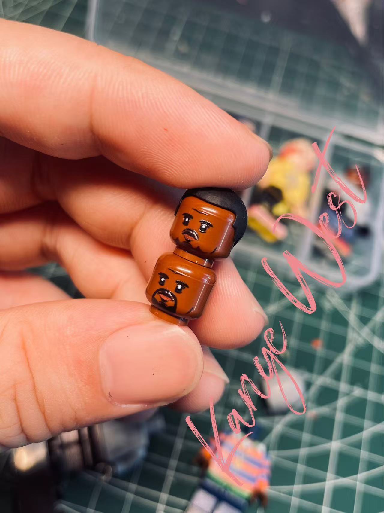 Kanye West custom minifigure heads, showcasing detailed facial designs; one with beard, held by hand.